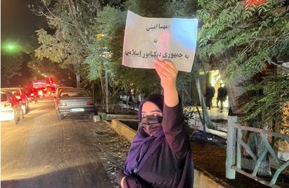 یک زن محجبه با چادر در یکی از خیابان‌های تهران پلاکاردی با شعار «نه به جمهوری دیکتاتور اسلامی» در دست دارد.