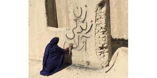 زنی بلوچ بر دیواری کاهگلی شعار مدرن و فراگیر «زن، زندگی، آزادی» می نویسد