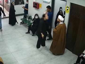 The footage shows a woman without a headscarf seeking medical attention for her child at a clinic in central Qom. The cleric is seen filming her with his phone