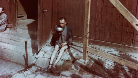 An emaciated survivor drinks from a metal bowl in front of a barracks in the newly liberated Buchenwald concentration camp. Spring 1945. Image Source: National Archives and Records Administration, College Park