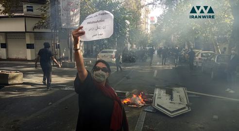 در جریان اعتراضات سراسری ۱۴۰۱ دختری بدون حجاب اجباری در کنار معترضین کاغذی که روی آن «زن، زندگی، آزادی» و «مهسا امینی» نوشته شده است را نشان می‌دهد. تهران