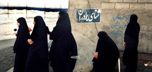 Iranian women look at men swimming in the Caspian Sea. The sign says, "Brothers' Swimming Area."  