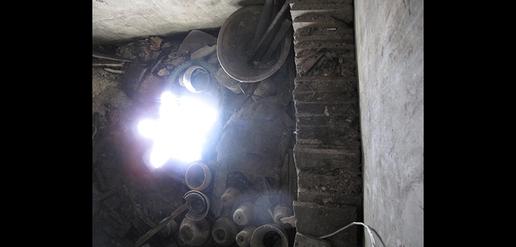 In a dark room with a collapsed floor, a blinking light in the basement warns the viewer