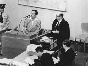 شهادت یک عکاس در دادگاه آیشمن  «هنریک روس» در دادگاه آیشمن حاضر شد و شهادت داد. او که عکاس رسمی سازمان آمار گتوی ووچ بود، مخفیانه از صحنه‌هایی از زندگی در گتو عکاسی کرده بود. فرد سمت راست «روس» در عکس، گیدئون هاوزنر، دادستان ارشد دادگاه است که تعدادی از عکس‌های او را به‌ عنوان سند و مدرک در دست دارد. ۲ مه ۱۹۶۱.