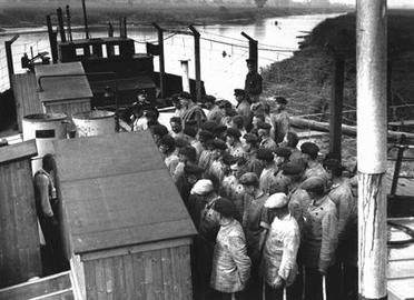 یک اردوگاه‌ اولیه کار اجباری بسیاری از اردوگاه‌های اولیه کار اجباری سرهم‌بندی‌شده بودند. این صحنه‌ای است از برگزاری مراسم حضور و غیاب زندانیان سیاسی در یک کشتی که از آن به‌عنوان اردوگاه شناور استفاده می‌شد. اردوگاه اوختومزاند، حوالی برمن، آلمان، ۱۹۳۳ یا ۱۹۳۴. مرکز اسناد دولتی برمن