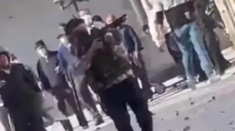 یک مامور مسلح جمهوری اسلامی که جلیقه ضدگلوله به تن دارد، در حال شلیک با سلاح جنگی به معترضان غیرمسلح در یکی از شهرهای ایران